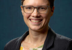 Portrait of Liz Lucas smiling, wearing a blazer against a blue background