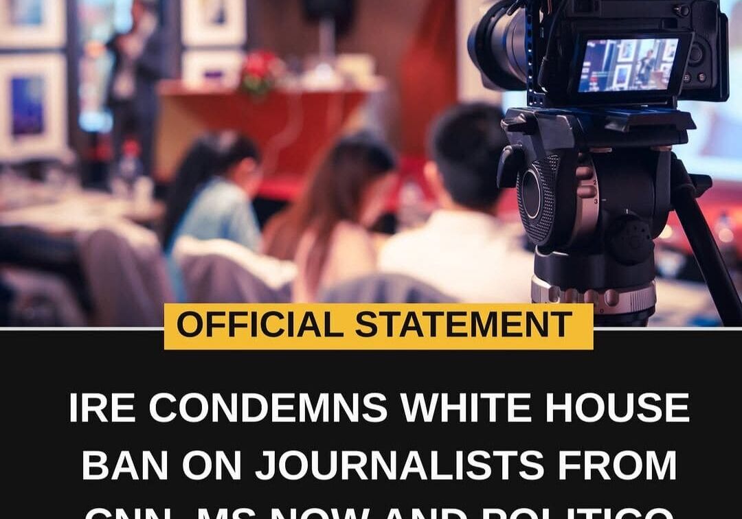 Official statement: IRE condemns white house ban on journalists from cnn, ms now and politico. Image shows a video camera in the foreground, points at a group of people in the background.